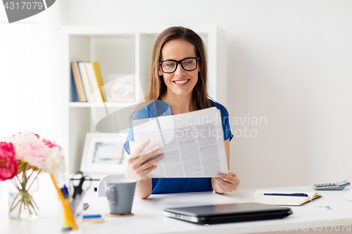 Image of happy woman in glasses reading newspaper at office