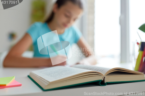 Image of girl with book writing at home