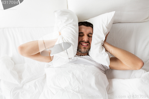 Image of man in bed with pillow suffering from noise