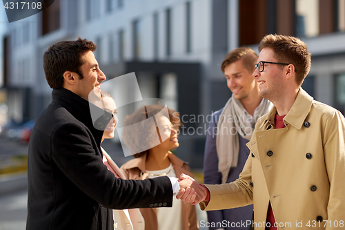 Image of happy people shaking hands on city street