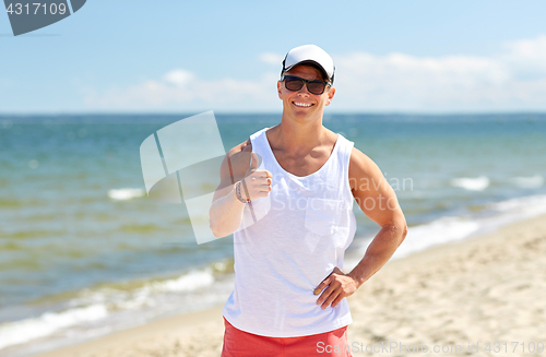 Image of smiling man on summer beach showing thumbs up