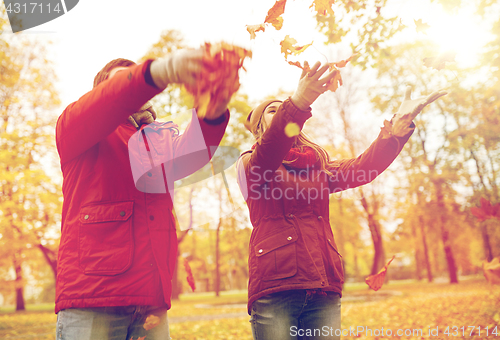 Image of happy young couple throwing autumn leaves in park