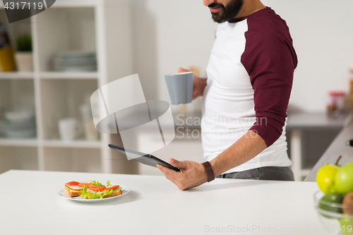 Image of man with tablet pc eating at home kitchen