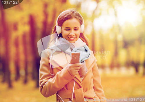 Image of woman with smartphone and earphones in autumn park