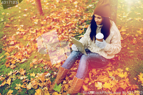 Image of woman with tablet pc and coffee in autumn park