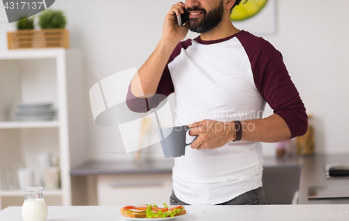 Image of man calling on smartphone and eating at home
