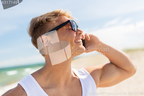 Image of smiling man calling on smartphone on summer beach