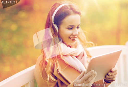 Image of woman with tablet pc and headphones in autumn park