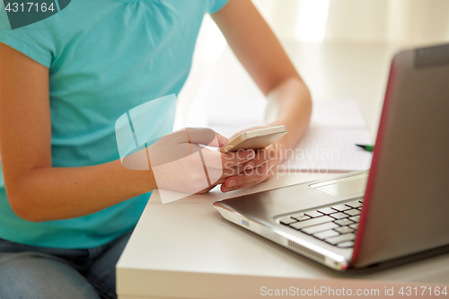 Image of girl with laptop and smartphone texting at home