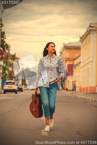 Image of beautiful woman with a guitar walking down the street