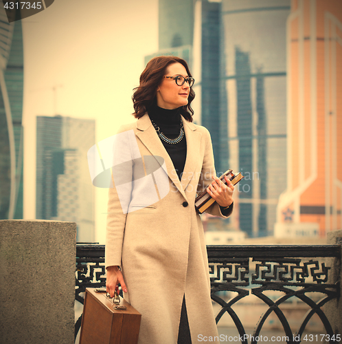 Image of smiling woman in a light coat with a briefcase and books