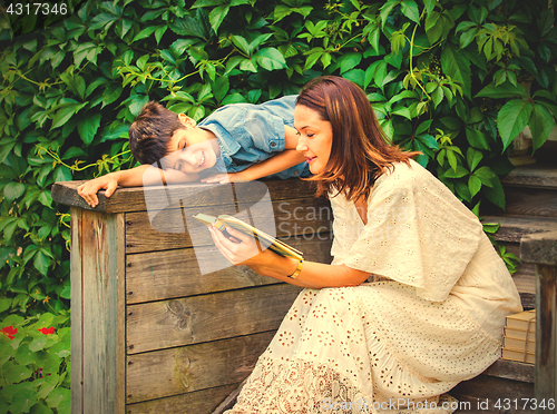 Image of woman and a boy are reading a book on an ancient wooden porch