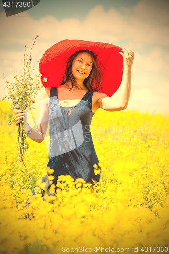 Image of woman with a bouquet in a red hat on a sunny day amidst wildflow