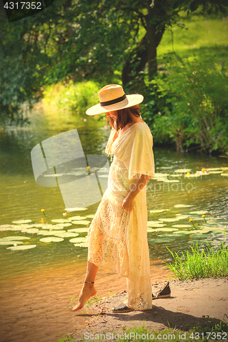 Image of beautiful european woman in a white dress and in a hat dips her 