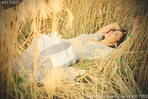 Image of beautiful woman in a white dress lies in the ears of corn