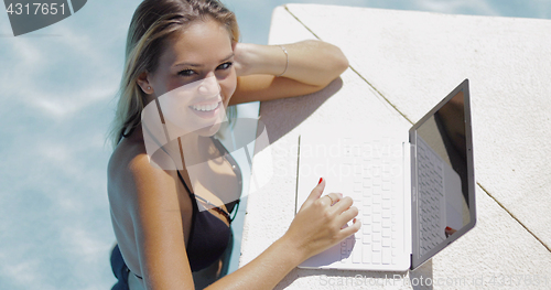 Image of Smiling woman relaxing in pool with laptop