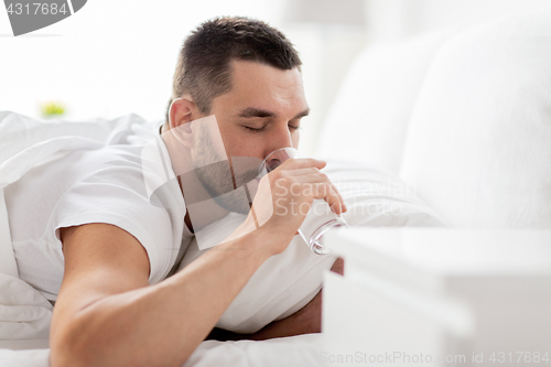 Image of man in bed with glass of water drinking at home