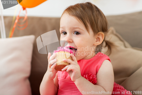 Image of happy baby girl eating cupcake on birthday party