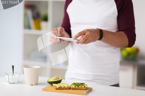 Image of man photographing food by smartphone at home