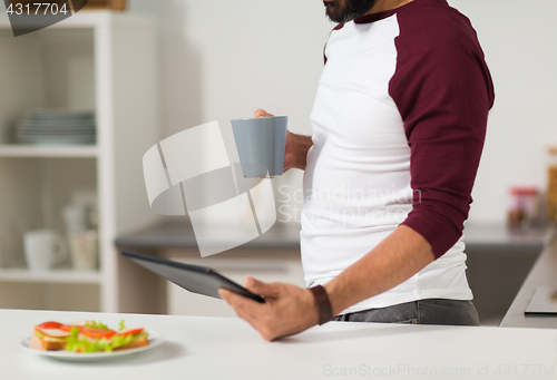 Image of man with tablet pc eating at home kitchen