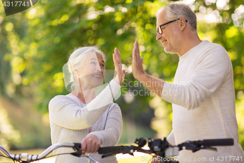 Image of senior couple with bikes making high five at park