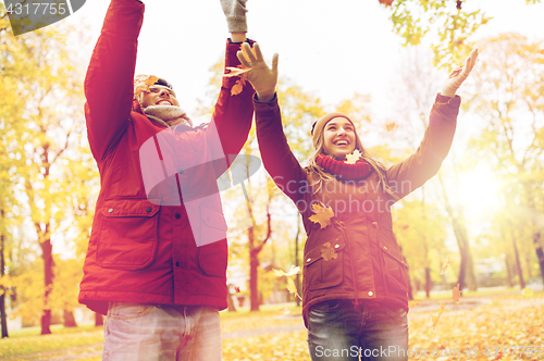 Image of happy young couple throwing autumn leaves in park