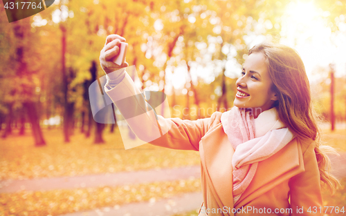 Image of woman taking selfie by smartphone in autumn park