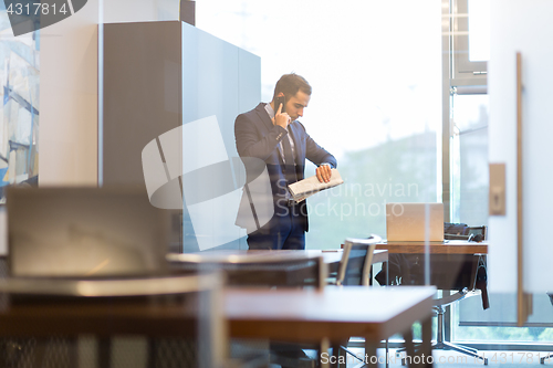 Image of Businessman talking on mobile phone while looking at wristwatch.