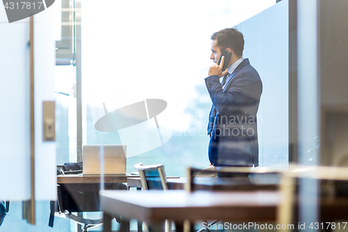 Image of Businessman talking on a mobile phone while looking through window.