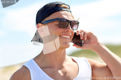 Image of smiling man calling on smartphone on summer beach