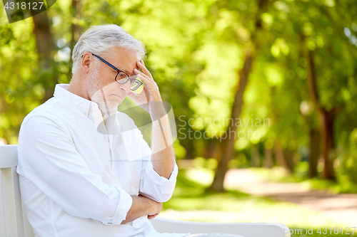 Image of thoughtful senior man sitting at summer park