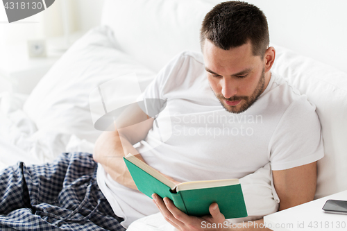 Image of man reading book in bed at home