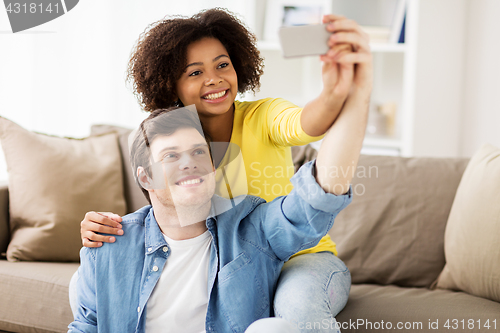 Image of happy couple with smartphone taking selfie at home