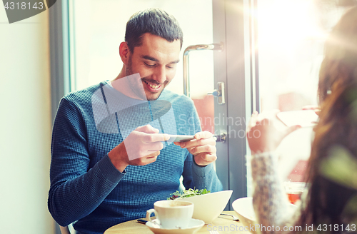 Image of happy couple picturing food by smartphone at cafe