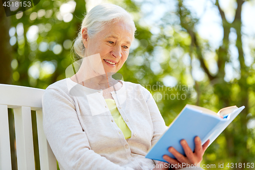 Image of happy senior woman reading book at summer park