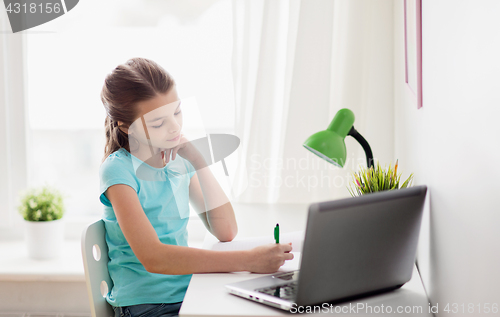 Image of girl with laptop writing to notebook at home