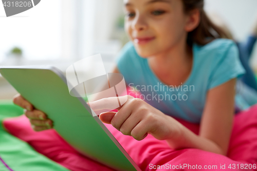Image of smiling girl with tablet pc lying on bed at home