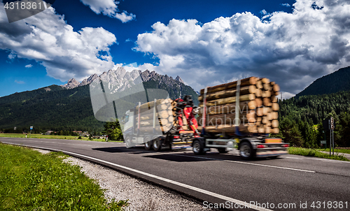 Image of Timber truck rushes down the highway in the background the Alps.