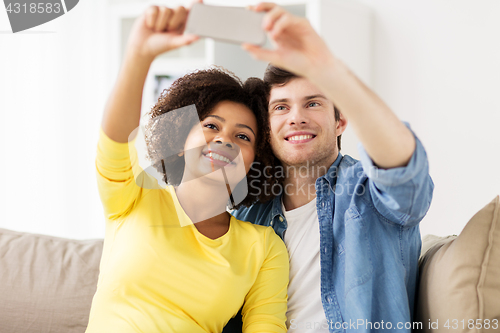 Image of happy couple with smartphone taking selfie at home