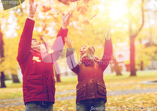 Image of happy young couple throwing autumn leaves in park