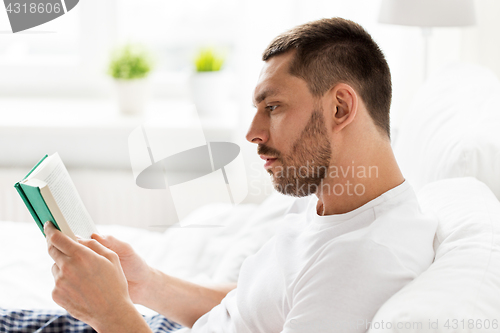 Image of man reading book in bed at home