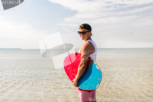 Image of happy young man with skimboard on summer beach