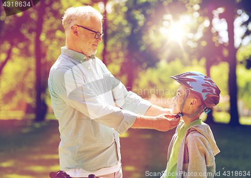 Image of old man helping boy with bike helmet at park