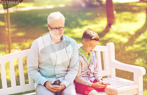 Image of old man and boy with smartphones at summer park