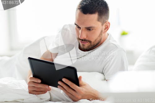 Image of young man with tablet pc in bed at home bedroom