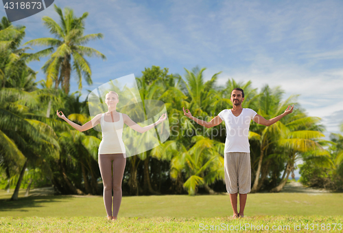 Image of happy couple making yoga exercises on beach