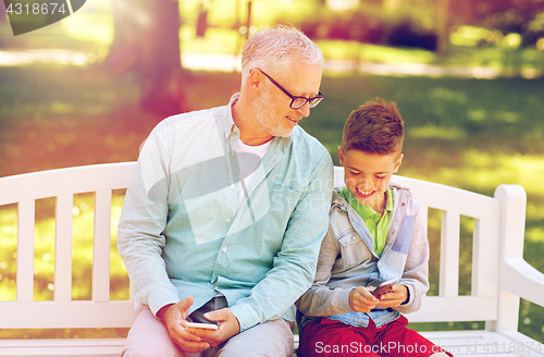 Image of old man and boy with smartphones at summer park