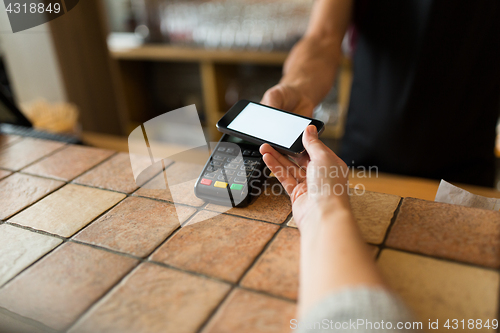 Image of hands with payment terminal and smartphone at bar