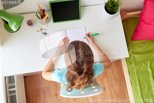 Image of girl with tablet pc writing to notebook at home