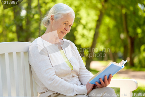 Image of happy senior woman reading book at summer park